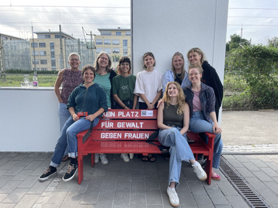 Eine Frauengruppe hat sich um eine rote Sitzbank versammelt